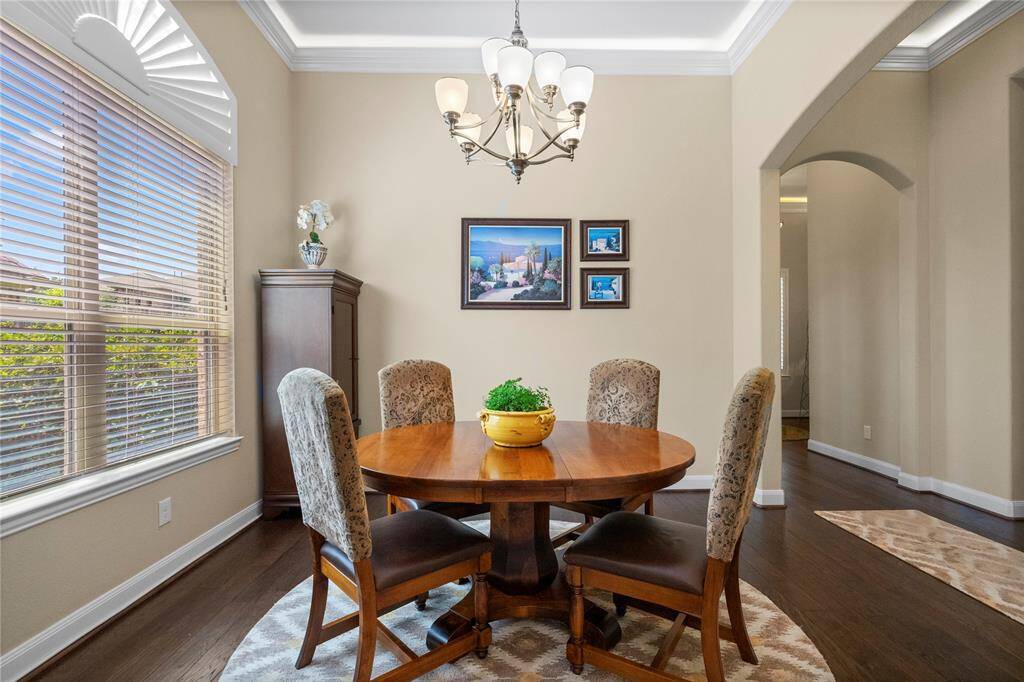 This dining area features elegant crown molding and a stylish chandelier. Large windows with blinds provide natural light, while an archway leads to adjacent spaces, enhancing the home's open feel.