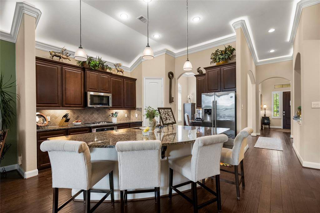 This kitchen features elegant dark wood cabinets, a spacious granite island with seating, and modern stainless steel appliances. The high ceilings, recessed lighting, and open layout create a welcoming and airy atmosphere, ideal for entertaining.