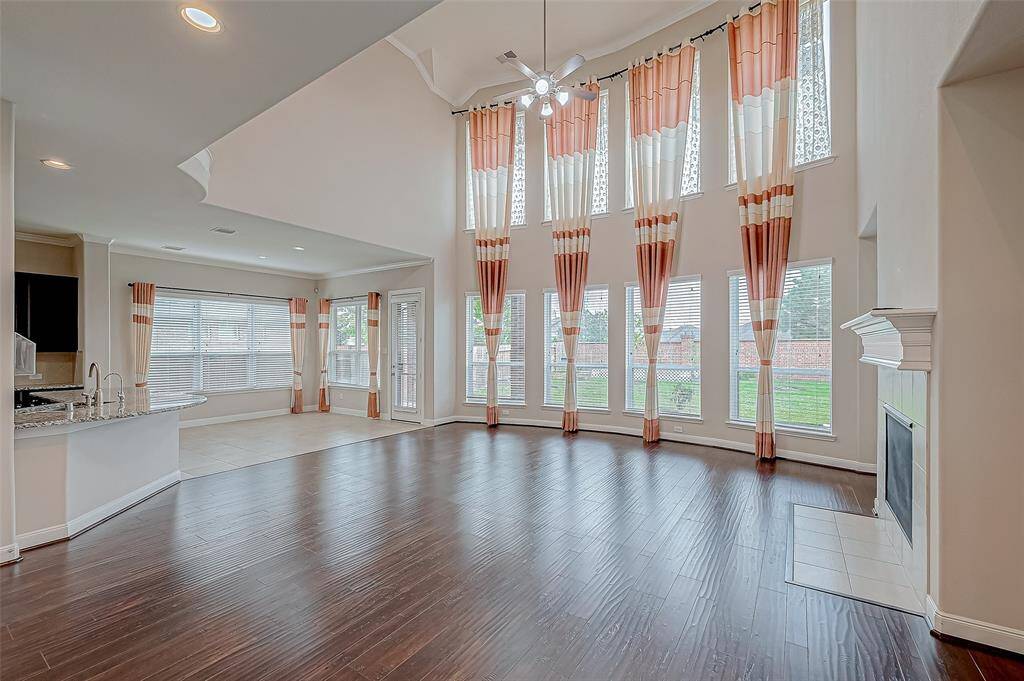 The living room features soaring high ceilings, complemented by four columns of long, regular windows that flood the space with natural light. A wood-finished fireplace adds a warm, inviting touch to this spacious and stylish area.
