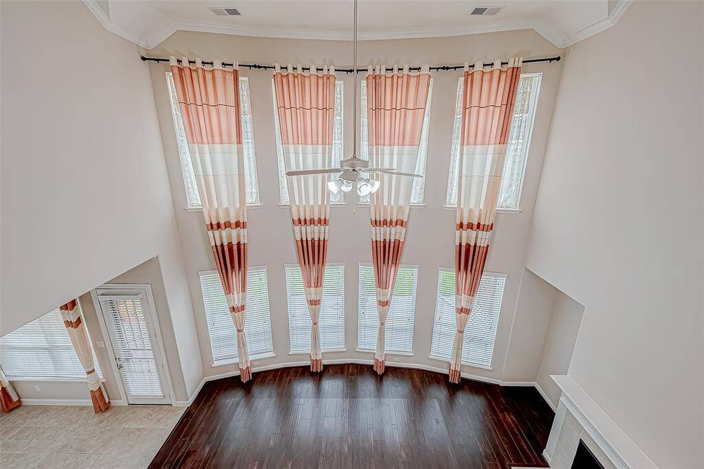 The living room features soaring high ceilings, complemented by four columns of long, regular windows that flood the space with natural light. A wood-finished fireplace adds a warm, inviting touch to this spacious and stylish area.
