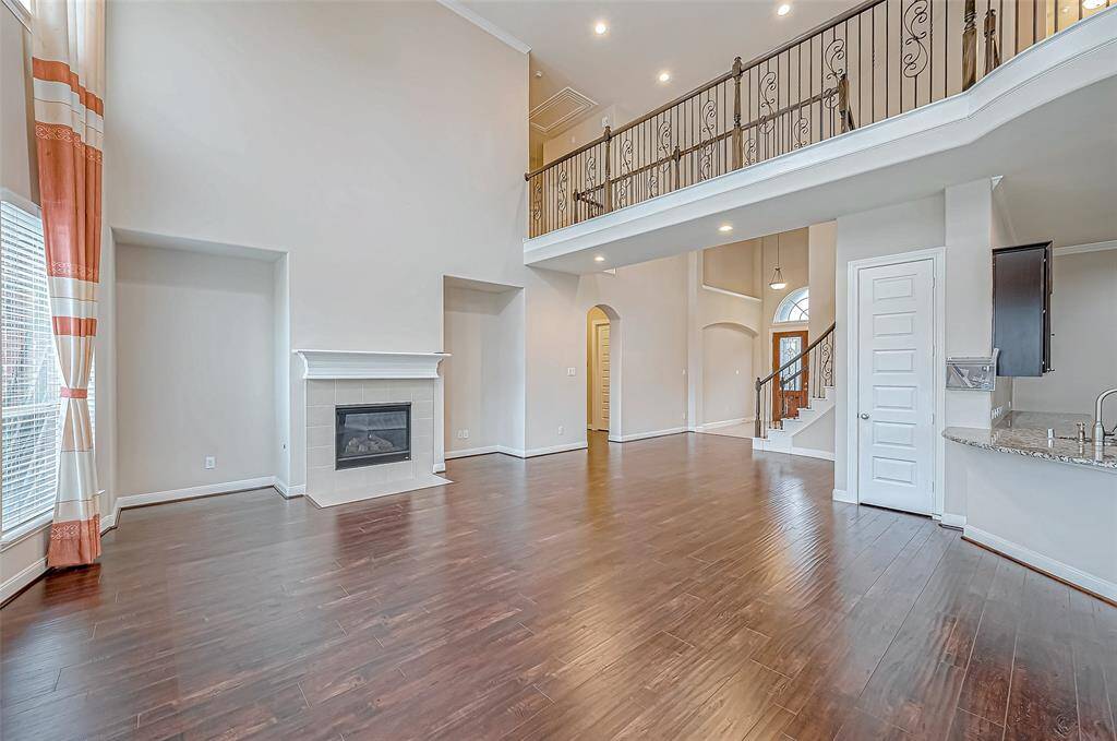 The living room features soaring high ceilings, complemented by four columns of long, regular windows that flood the space with natural light. A wood-finished fireplace adds a warm, inviting touch to this spacious and stylish area.