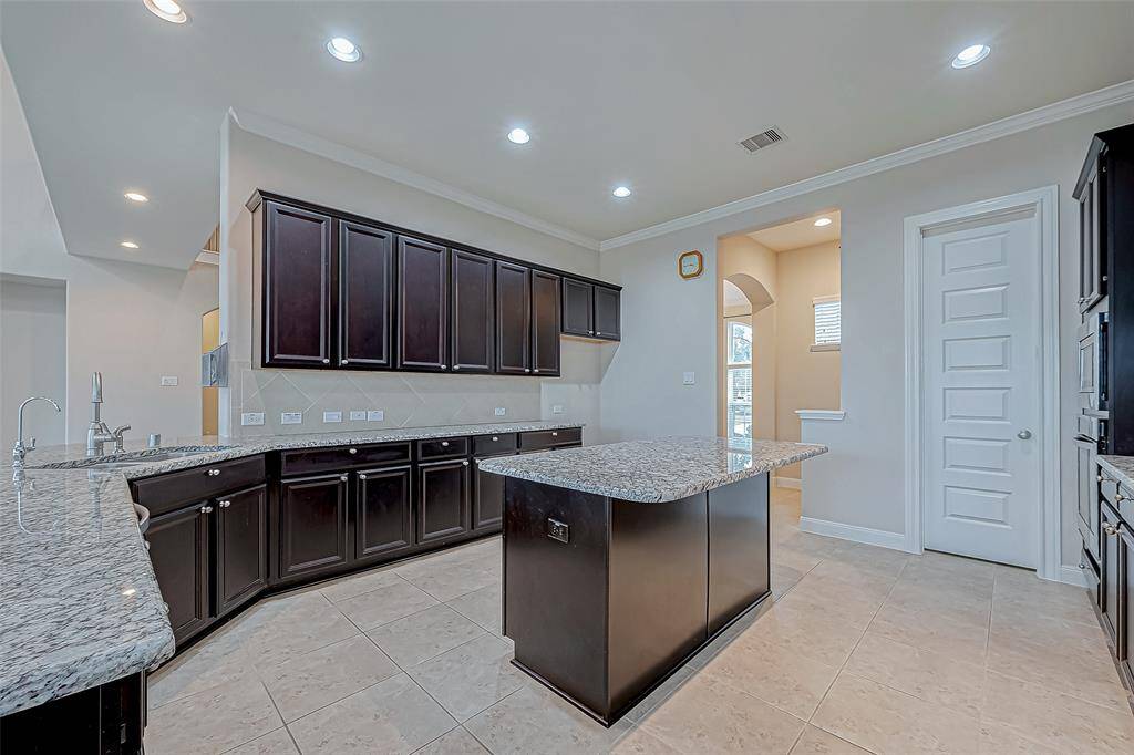 The kitchen features stunning granite countertops, including a central island that adds both functionality and style. Dark wood cabinets provide a rich contrast, creating an elegant and inviting cooking space.