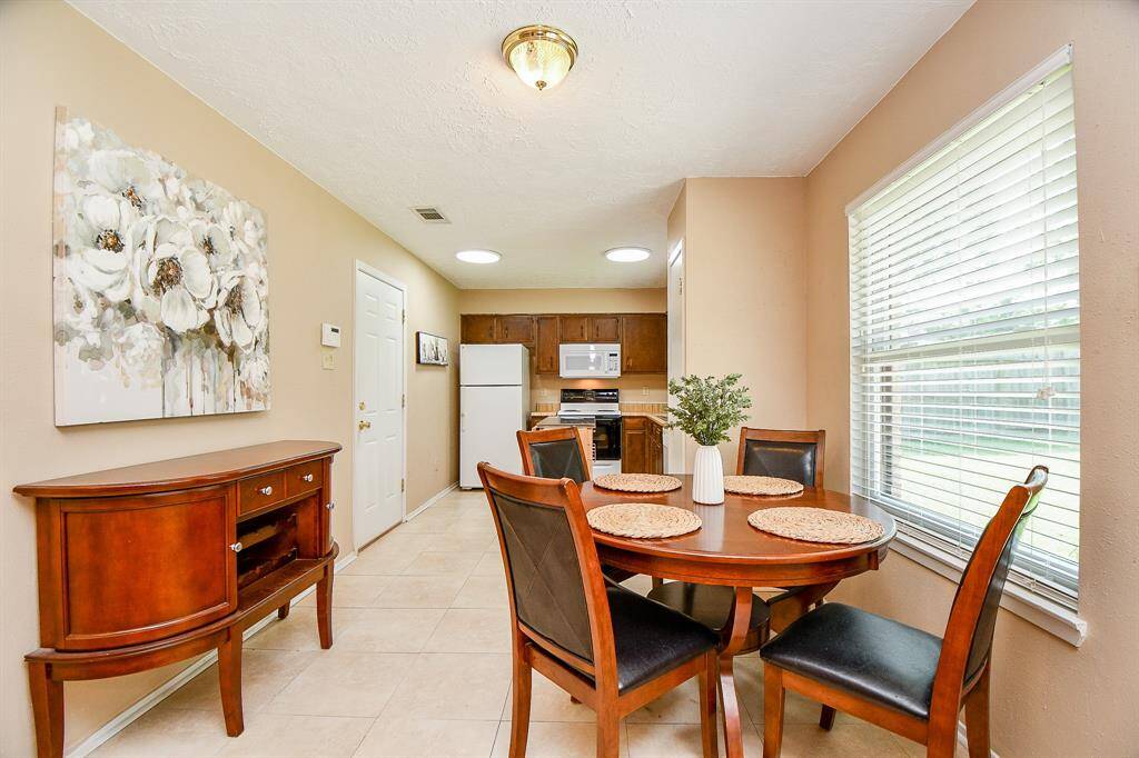 Photo showcases a dining area situated next to a large window for natural light. The space leads into the kitchen with ample cabinet storage, counter tops, and pantry.