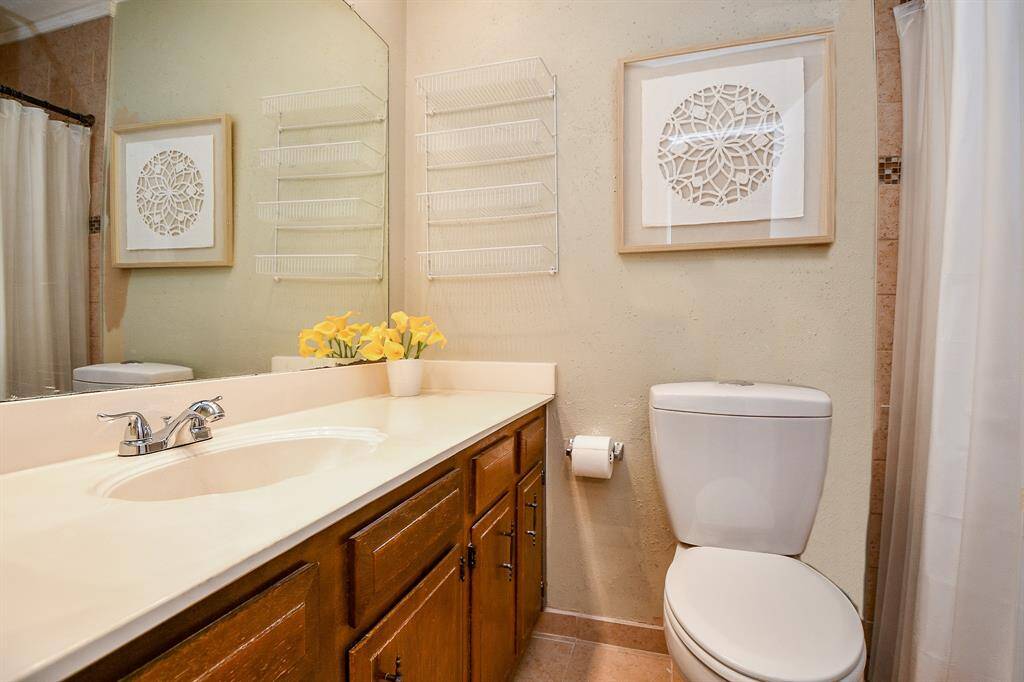 Primary bathroom features a clean design with a white countertop, wooden cabinets, sink, an updated toilet, a shower with a curtain creating a functional space.