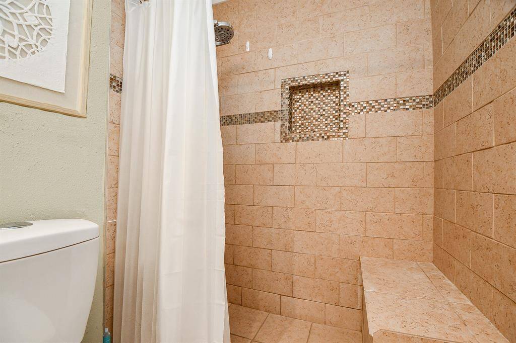 Primary ensuite bathroom with a tiled walk-in shower featuring a built-in bench and mosaic accent. Updated toilet.