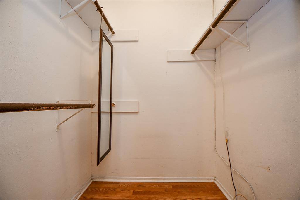 This photo shows a 5X5 walk-in closet with wooden flooring, white walls, and two shelves with hanging rods on either side. There's a full-length mirror attached to one rod, providing a functional space for clothing storage and dressing.