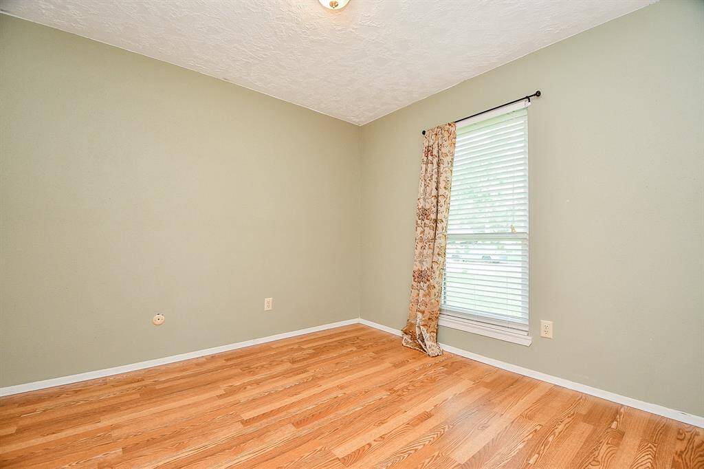 This 2nd bedroom features light green walls, hardwood flooring, a window with blinds and floral curtains, just off hall with convenient linen closet.