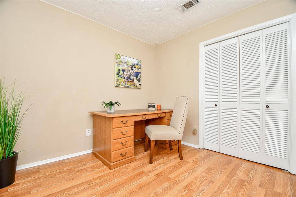 3rd bedroom with a closet with louvered doors. The room features hardwood floors, and neutral walls,.and a touch of greenery, creating a warm and inviting workspace.