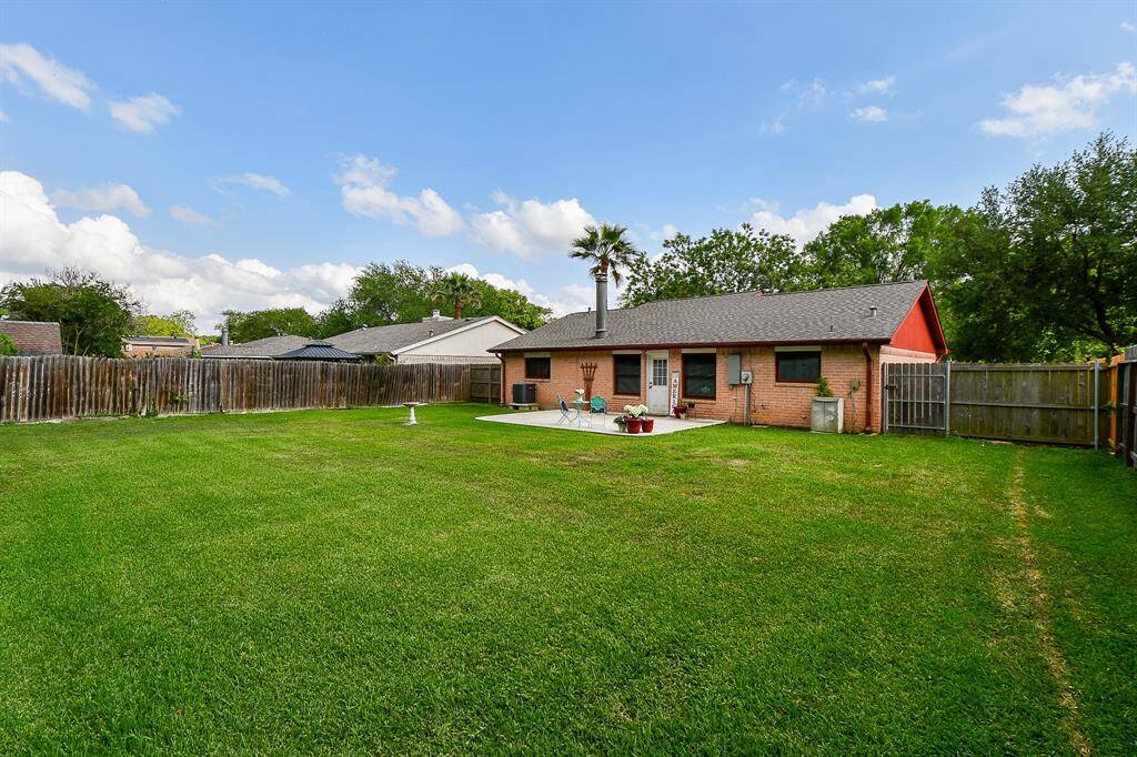Spacious backyard featuring a well-maintained lawn, a cozy brick house with a patio area, and a wooden fence for privacy. Ideal for outdoor activities and relaxation.