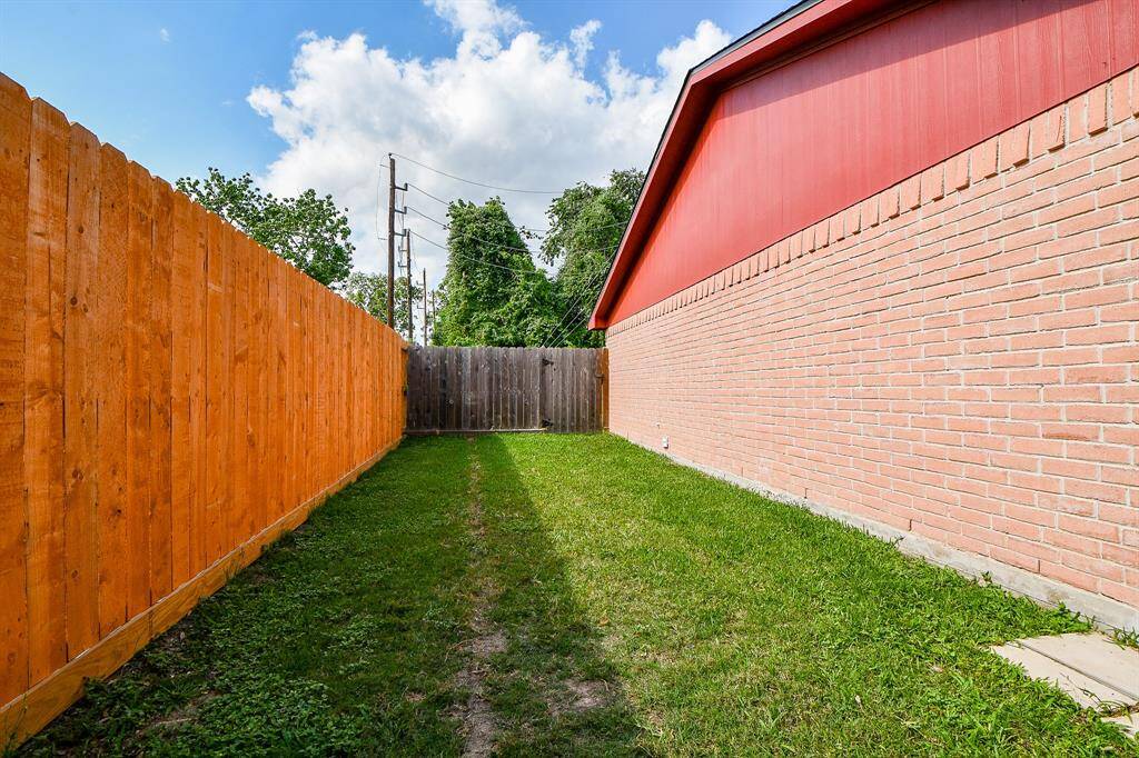 Separately Fenced Side yard with a well-maintained grassy area, bordered by a wooden fence on one side and a red brick wall on the other. Perfect for a small garden, furry pets, or outdoor storage.