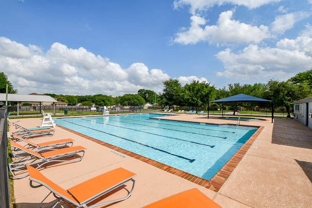 Spacious outdoor swimming pool area with lane lines, surrounded by a sundeck with orange loungers, shaded seating, ideal for relaxation and recreation.
