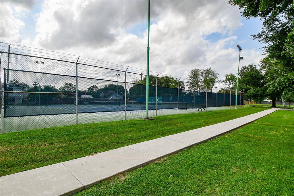 Tennis court surrounded by lush greenery and a walking path, perfect for outdoor activities in a peaceful residential area.