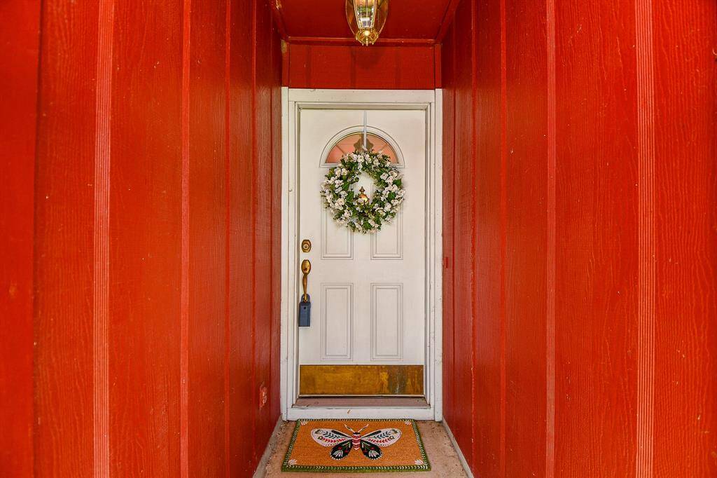 Welcoming entryway featuring a white upgraded front door with window, framed by vibrant red walls. A welcoming doormat adds a touch of personality, creating a cozy first impression.