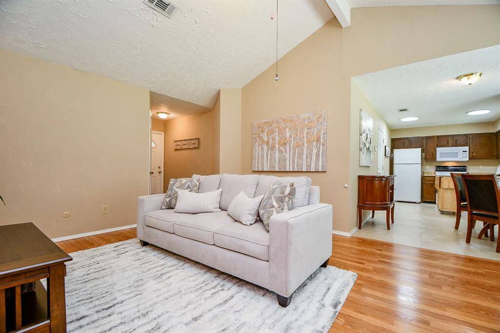 Primary Bedroom View of spacious living area f, features a neutral palette, wood flooring, and an open view into a well-lit kitchen. Ideal for comfortable living and entertaining.