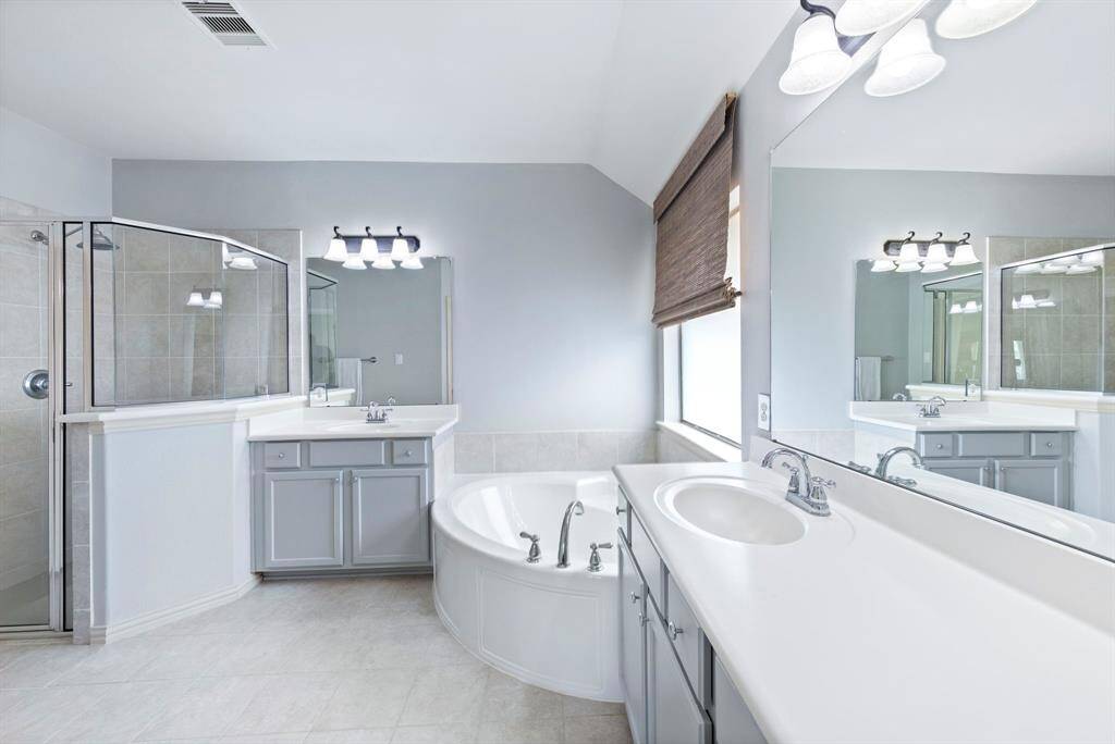 The primary bathroom offers a clean, airy feel with dual vanities, a large soaking tub, and a separate glass-enclosed shower.