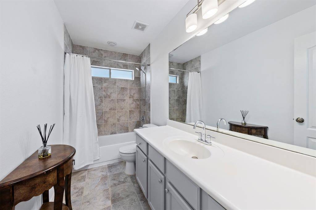 This secondary bathroom offers a clean, modern aesthetic with a tiled shower/tub combo, extended vanity, and ample storage.