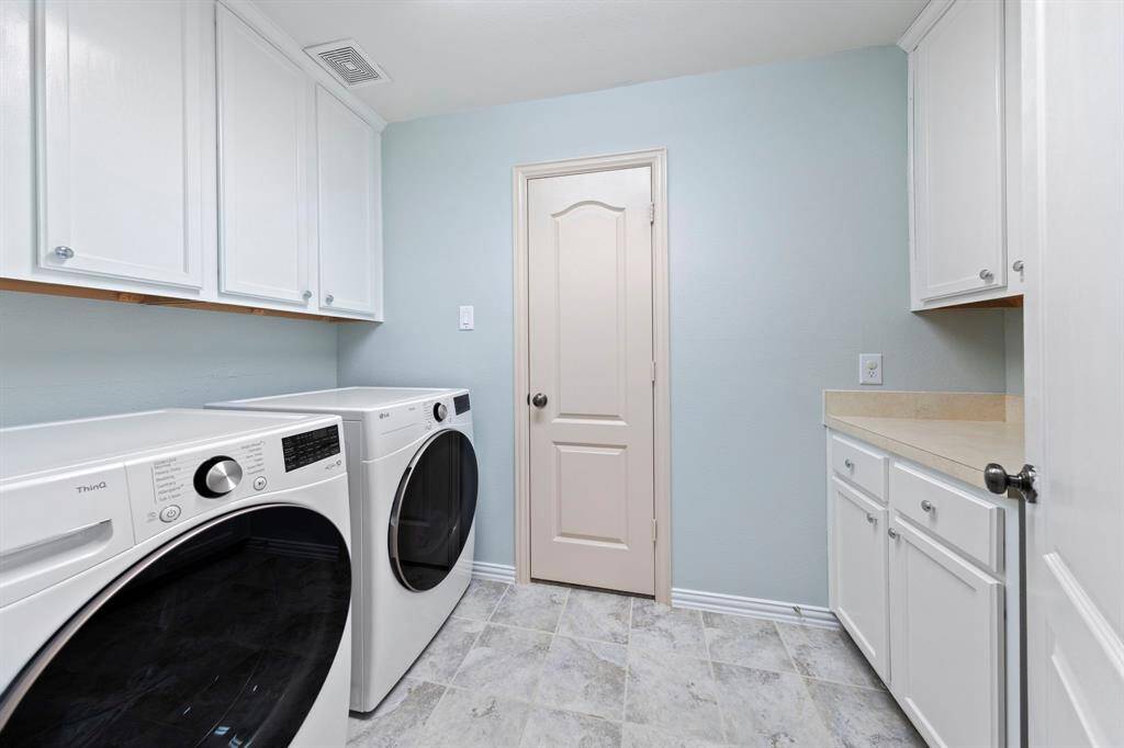 This bright and functional laundry room offers ample cabinet storage, tile flooring, and generous counter space for folding and organization.