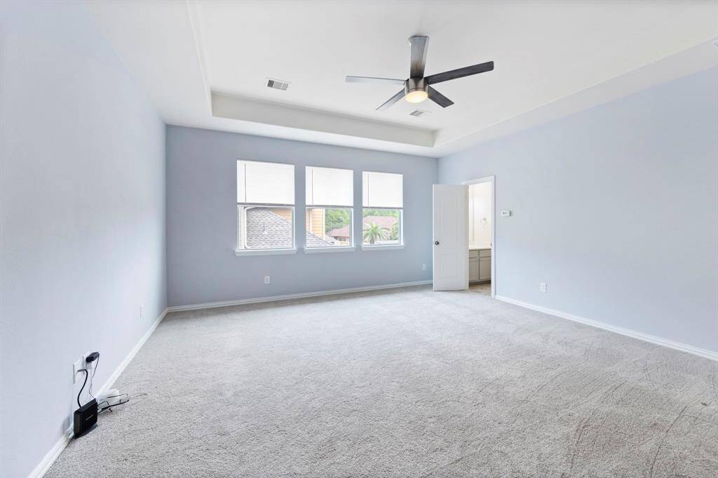 Bright and airy upstairs game room with plush carpet, tray ceiling, sleek fan, and triple windows for abundant natural light—complete with a half bathroom.