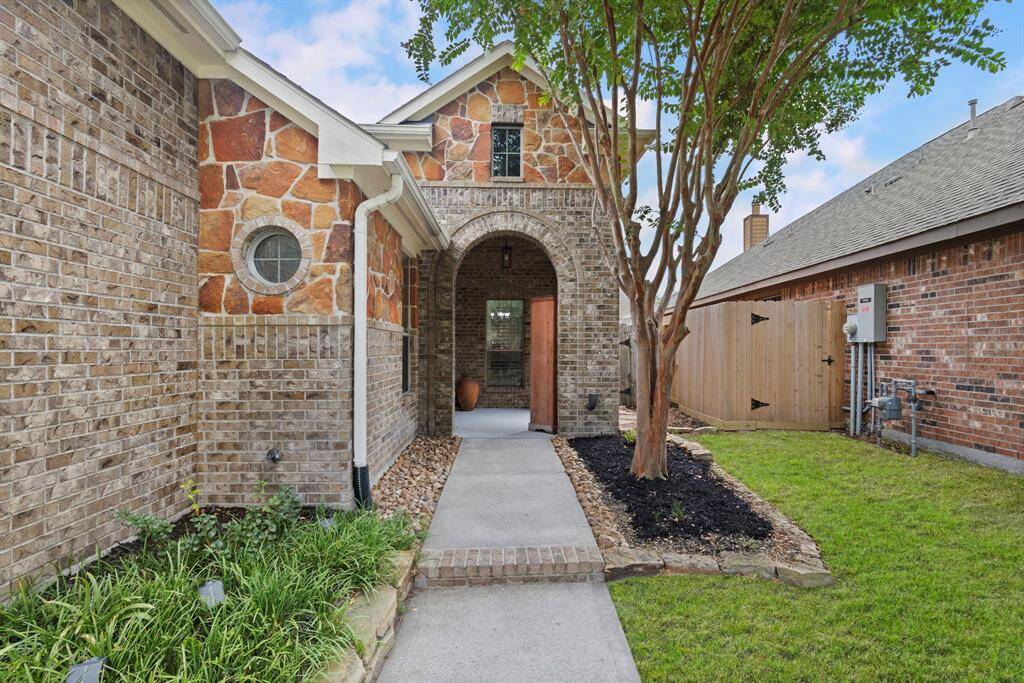 A charming stone-accented entryway with a graceful arched porch and manicured landscaping sets a warm and welcoming tone.