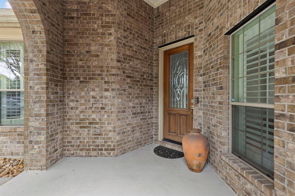 The inviting front door features elegant leaded glass detailing, set within a cozy brick-lined porch perfect for welcoming guests.