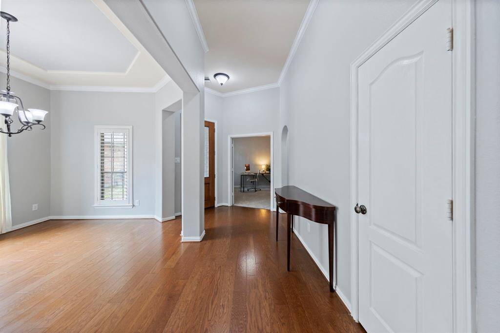 The entryway features warm wood floors, elegant crown molding, and a view into the formal dining area and home office—creating a bright, welcoming first impression.