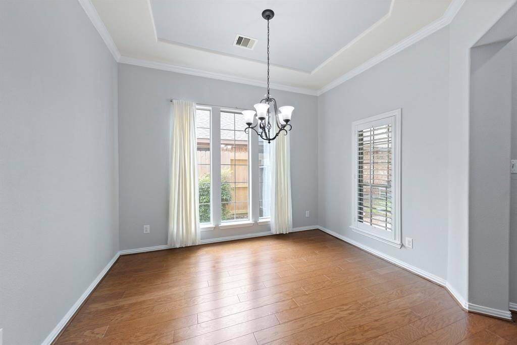 The dining room is bright and airy, featuring rich hardwood flooring, chandelier, and large windows with plantation shutters that let in abundant natural light.