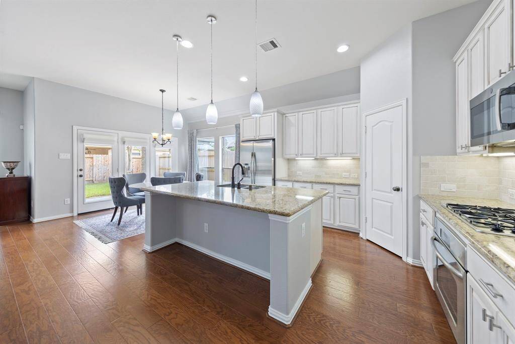 Sunlit kitchen featuring a gleaming granite island, sleek stainless-steel appliances, crisp white cabinetry, and a charming breakfast nook with inviting views of the backyard.
