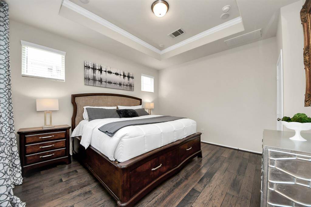 This primary bedroom features a cozy atmosphere with a tray ceiling, hardwood floors, and ample natural light from two windows.