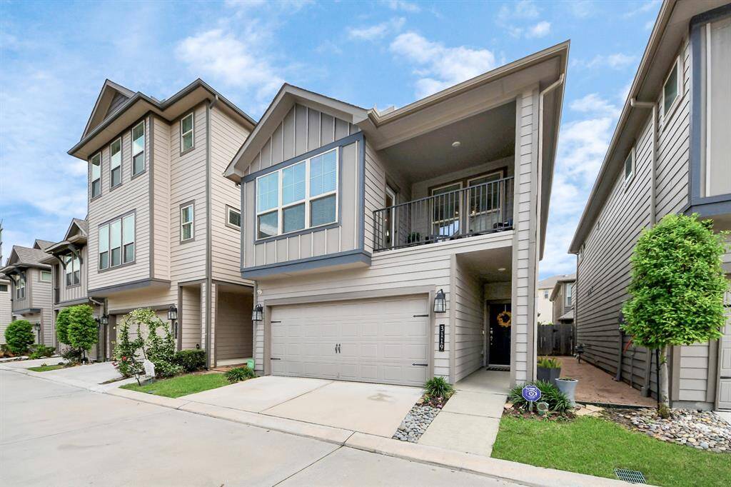 Modern townhouse with a two-car garage, featuring a small landscaped front yard and a welcoming entrance. The home has a covered balcony on the second floor, and the exterior is finished with sleek, neutral siding.
