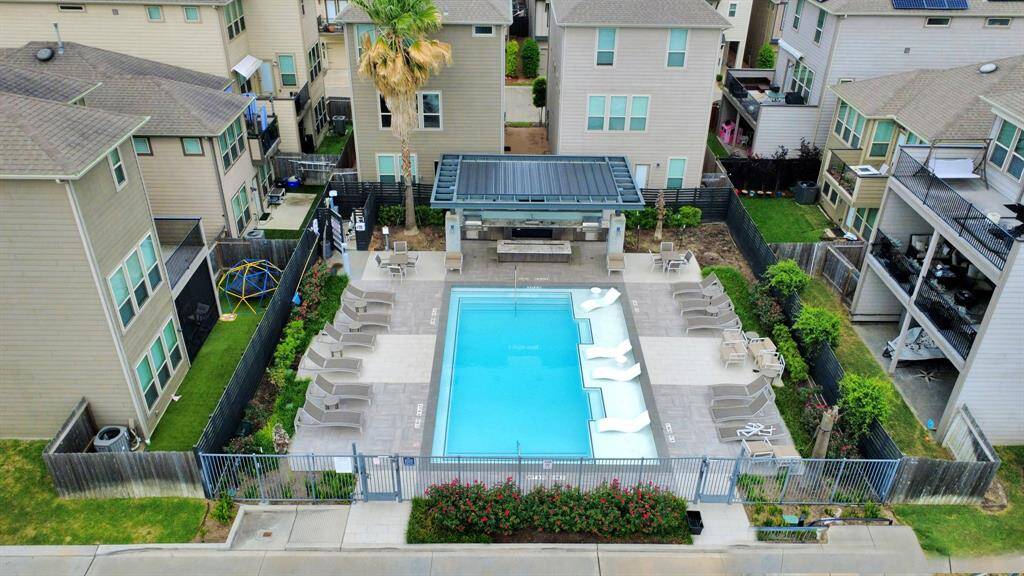 This photo shows a community swimming pool surrounded by modern homes. The pool area includes lounge chairs, a covered seating area, and is enclosed by a fence for privacy. It's a well-maintained, inviting space perfect for relaxation and social gatherings.