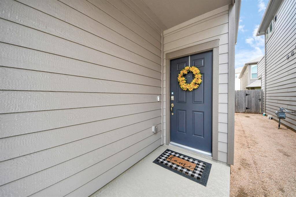 This modern, three-story townhouse features a two-car garage, a balcony, and a sleek exterior with neutral colors. It's situated in a tidy, well-maintained neighborhood with close-set homes and minimal landscaping.