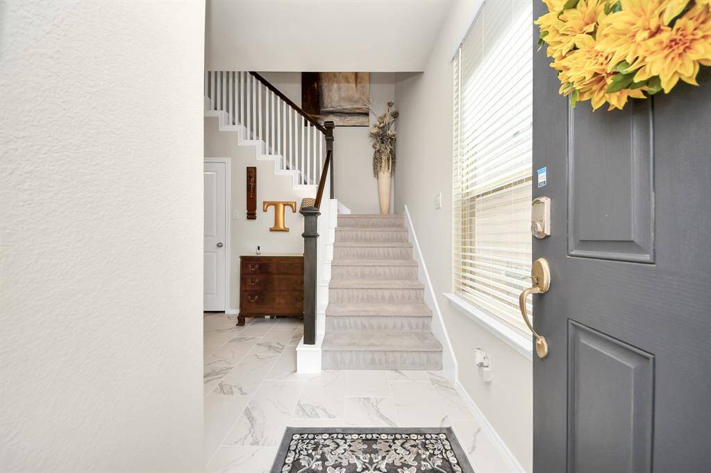 Welcome to your new home! This inviting entryway features a charming blue door adorned with a yellow floral wreath, a welcoming doormat, and a cozy covered porch area, perfect for greeting guests.