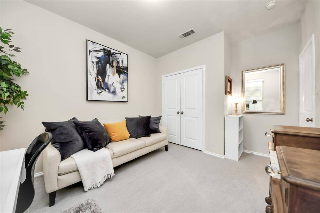This bright, cozy room features a small office setup with a desk and chair, a cream-colored sofa with accent pillows, large windows for natural light, and modern artwork on the wall. Perfect for a home office or study.