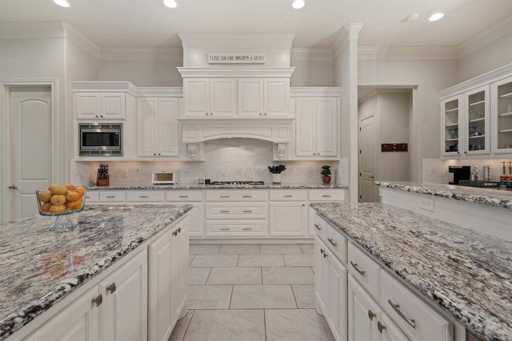 This classic white and bright Kitchen boasts upgraded granite countertops, white subway tile backsplash with accent tile, and brushed nickel hardware. The decorative range hood includes attractive corbel detailing and draws the eyes upward.