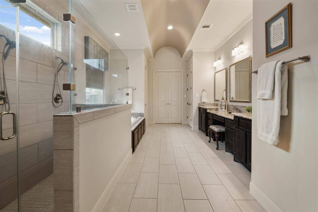 This Primary Bath is luxuriously appointed with an accented barrel ceiling, crown molding, and tile flooring. The double doors straight ahead lead into a large, walk-in closet adorned with built-in clothing racks, shoe racks, and a full-length mirror. To the right is a linen closet that can hold extra towels, linens, and toiletries.
