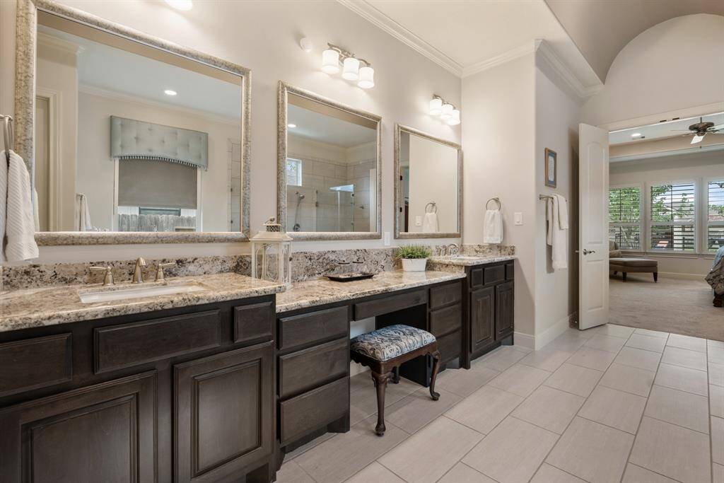 This long and spacious vanity boasts upgraded granite countertops, two undermount sinks, a central makeup vanity, and three custom framed mirrors.