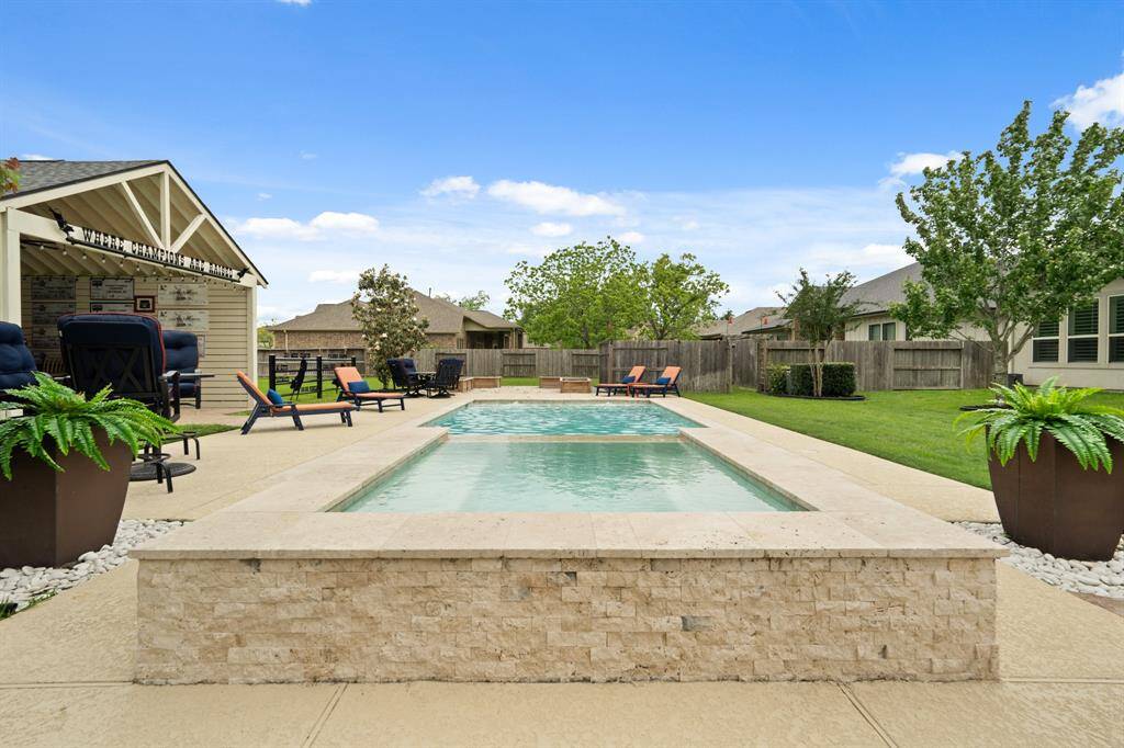 This elegant, raised Spa is finished with stacked stone surround and boasts a waterfall feature. Cool decking surrounds the Pool, providing cool and slip-free flooring. Notice the rock bed corners that provide a great spot to introduce foliage and a pop of color to the space.