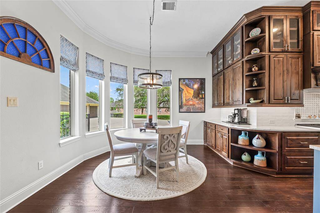 The elegant breakfast area, bathed in natural light from windows framing the picturesque backyard, is further elevated by a stunning designer pendant light, creating a serene and sophisticated setting for casual dining or morning coffee.