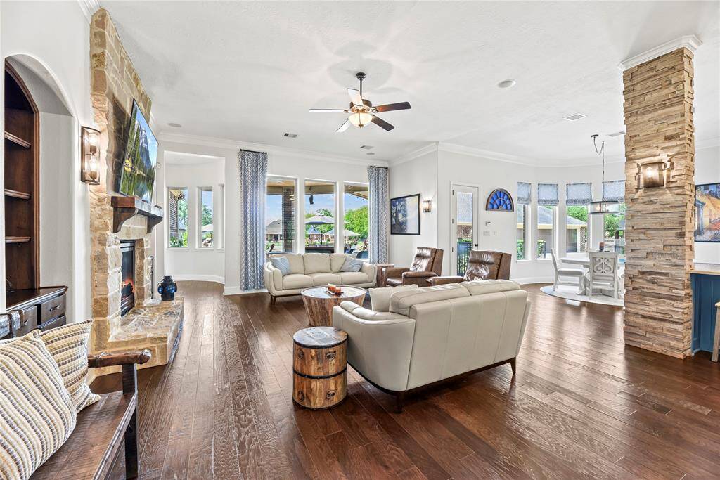The luxurious living area, seamlessly connected to the kitchen and breakfast room, showcases breathtaking views of the sparkling pool and features a striking stone-clad central fireplace, offering an elegant yet inviting space for relaxation and entertaining.