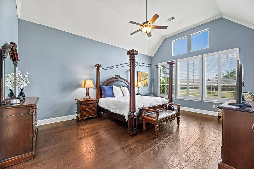 The luxurious primary suite boasts soaring vaulted ceilings and expansive windows that flood the space with natural light, while rich engineered wood flooring and elegant plantation shutters add warmth and sophistication to this serene retreat.
