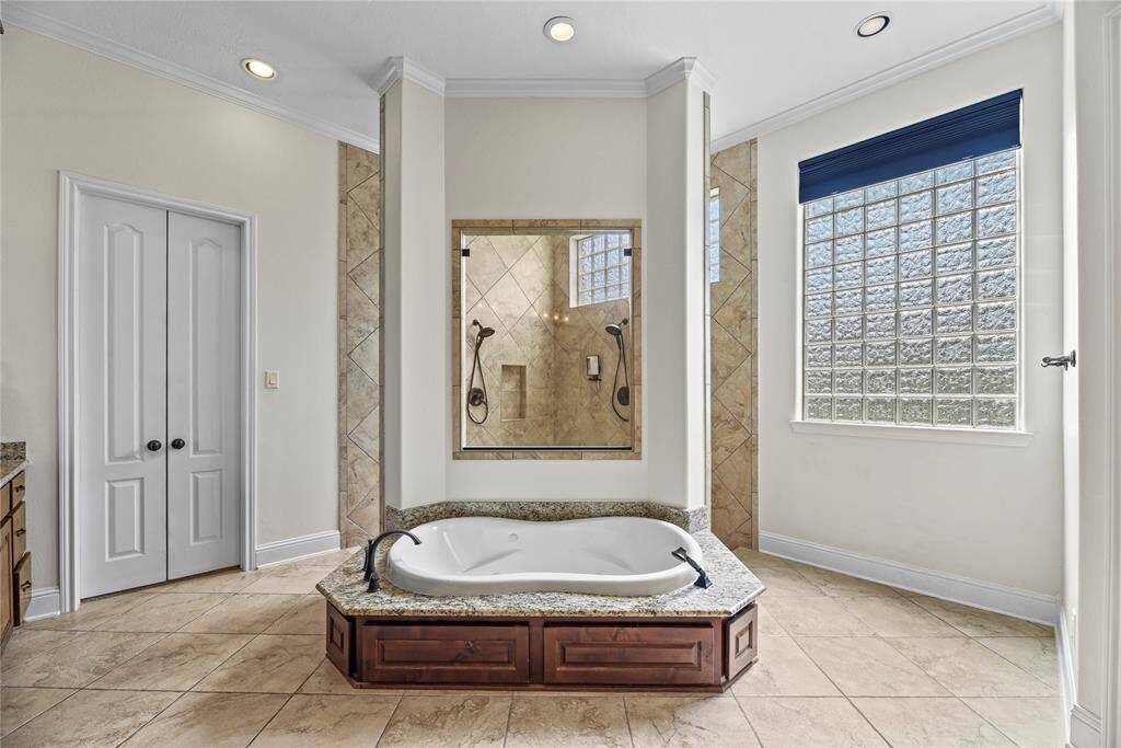 The deep soaking tub, set against a striking glass block window, offers a tranquil retreat infused with soft, natural light—perfect for unwinding in serene luxury.