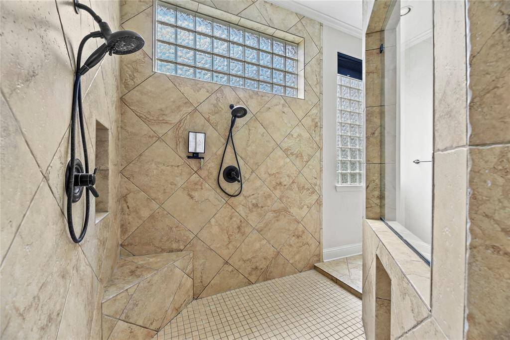 The expansive walk-in shower showcases exquisite tile craftsmanship and features dual shower heads for a truly indulgent, spa-inspired experience.