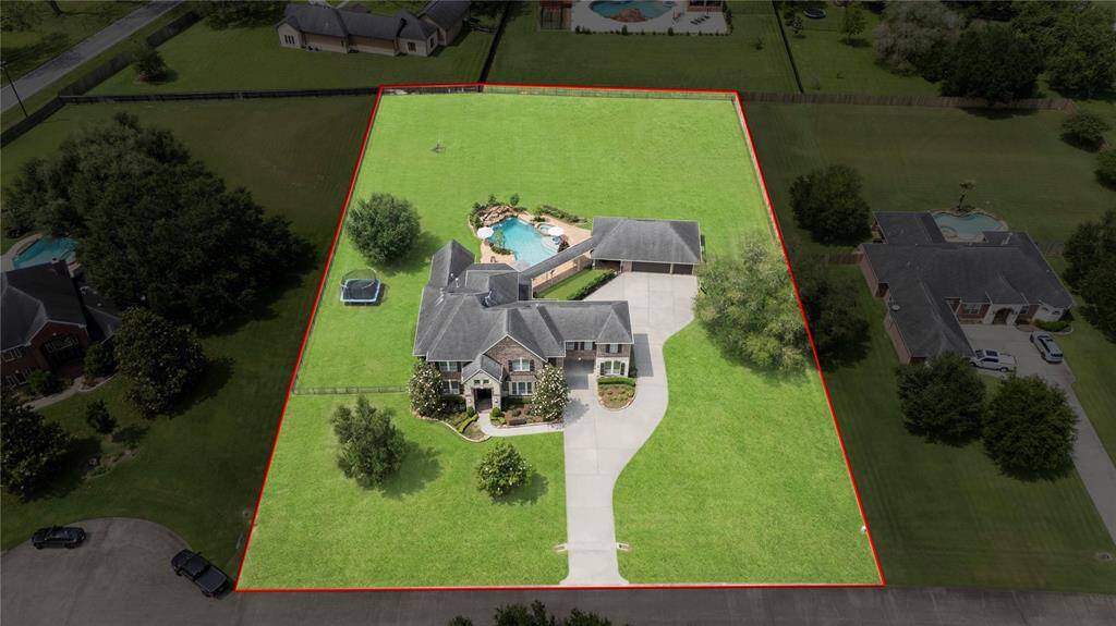 This breathtaking aerial shot highlights the magnificence of the expansive property, featuring a stunning luxury home, resort-style pool, and a grand four-car garage with an elegant porte-cochère—beautifully situated on a sprawling, manicured lot.