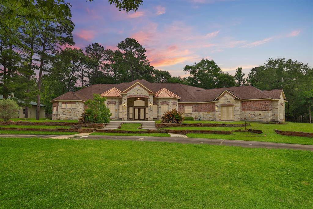 This photo showcases a beautiful, single-story brick and stone house with a spacious front lawn. The home features a large, inviting entrance and is surrounded by mature trees, offering a serene and picturesque setting.