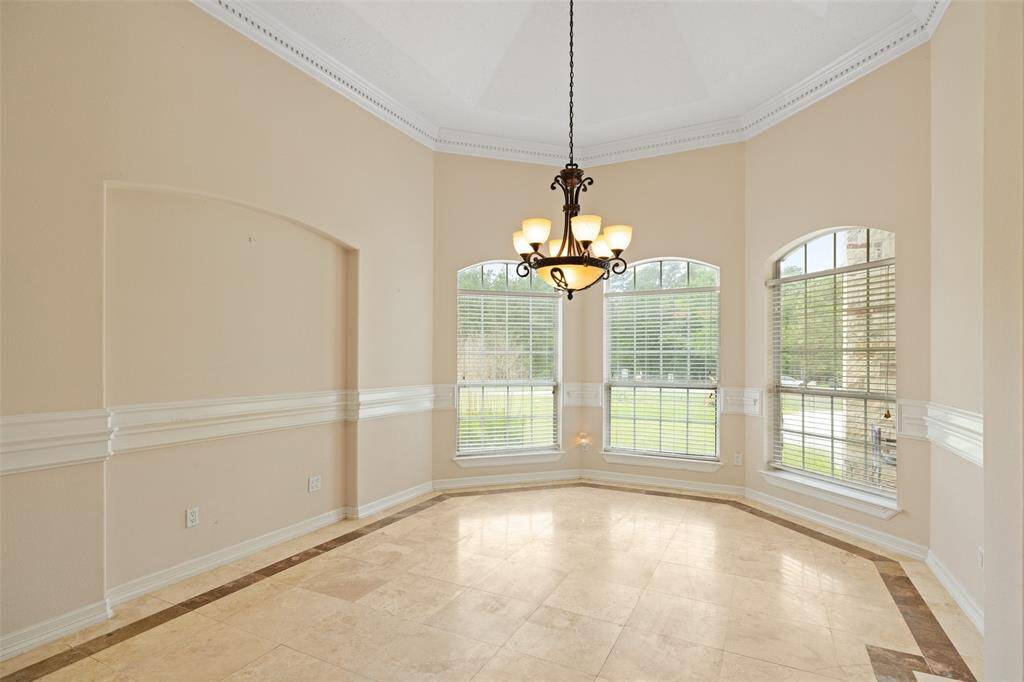 This dining room features large windows providing ample natural light, a stylish chandelier, and tile flooring. The neutral walls and crown molding add a touch of sophistication.