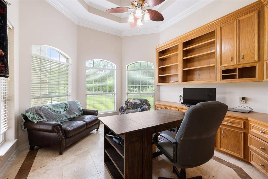 This bright home office features large windows, built-in wood cabinetry, and a ceiling fan. Ideal for getting your work done.