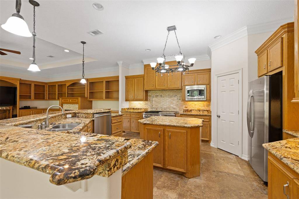 This spacious kitchen features elegant granite countertops, warm wooden cabinetry, and stainless steel appliances. It includes a large island, ample storage, and stylish lighting, perfect for cooking and entertaining.