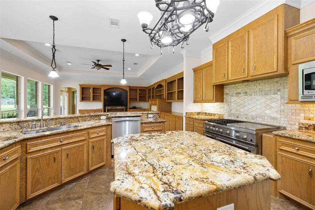 This spacious kitchen features granite countertops, ample wooden cabinetry, a large island, and modern stainless steel appliances. The open layout, with a view of the backyard through expansive windows, creates an inviting and functional space.