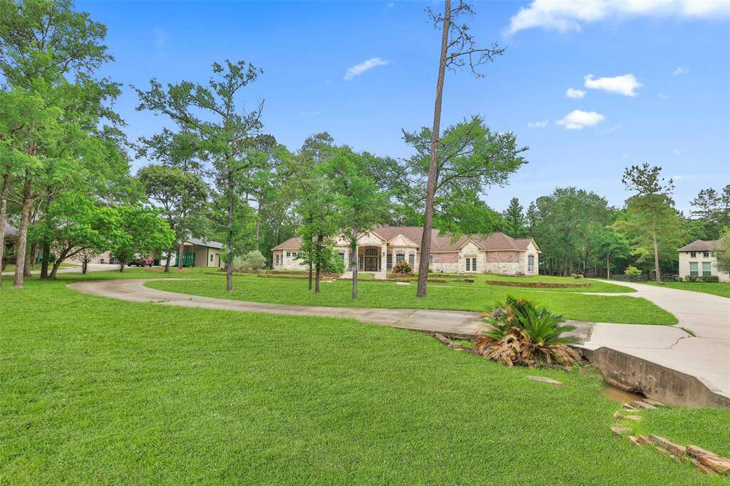This photo features a spacious, home set amidst lush greenery with a circular driveway. The house has a stone façade and is surrounded by mature trees, creating a serene and private setting.