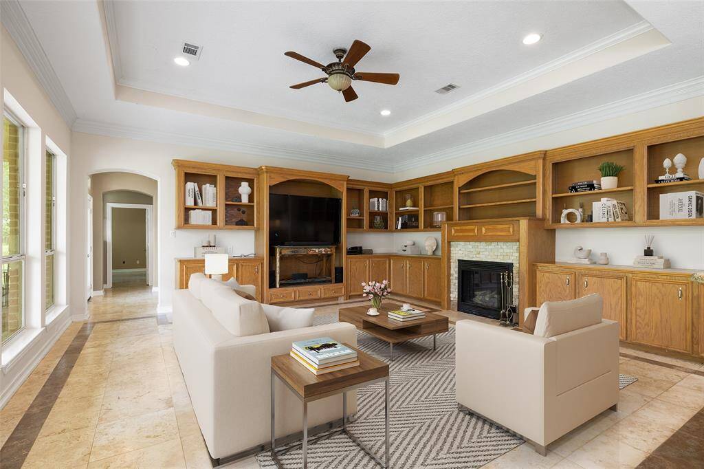 This spacious living room features a cozy fireplace, built-in wooden shelving, and tile flooring. Large windows provide ample natural light, while a ceiling fan and recessed lighting add comfort and style. Digitally staged for ideas for your living room furniture.